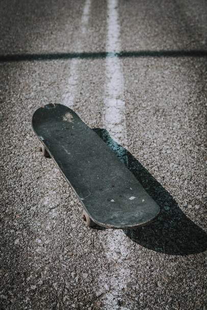A vertical shot of an old black skateboard on the concrete ground - 写真・画像