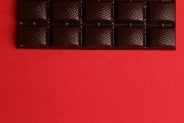 A high angle shot of a bar of dark chocolate isolated on a red surface - Foto, Bild