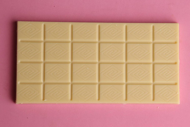 Вид сверху на плитку белого шоколада на розовой поверхности - Фото, изображение