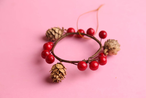 A closeup of a Christmas decoration with small pine cones and red balls on a pink surface - Photo, Image