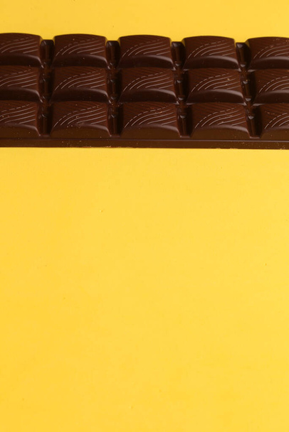 A vertical shot of a dark chocolate bar on yellow background - Foto, Bild