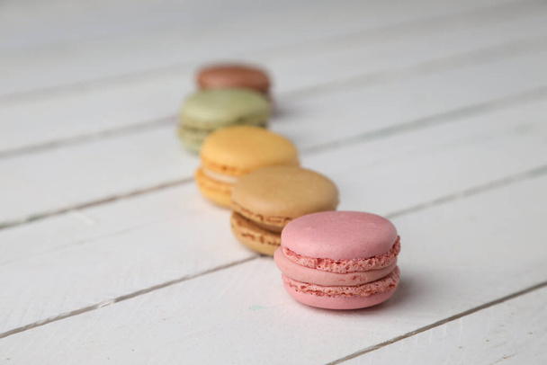 A selective focus shot of different flavors of macarons assorted on a white wooden surface - Fotografie, Obrázek