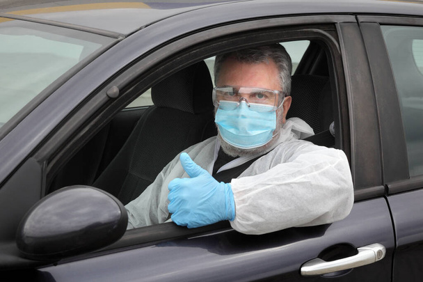 Adult driver with protective surgical mask glasses and gloves gesturing with thumb up from car, corona virus protected person - Foto, imagen