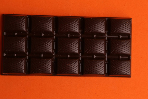 A high angle view of a dark chocolate bar isolated on an orange background - Fotó, kép