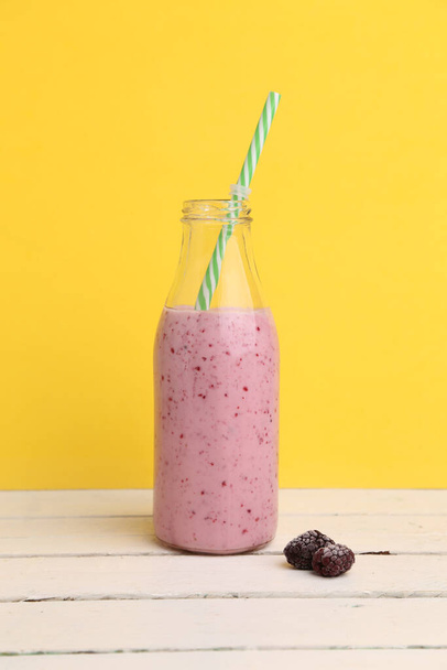 A strawberry smoothie in a bottle with frozen blackberries on the side - Фото, зображення