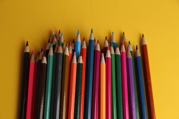 A high angle shot of a bunch of colored pencils on a yellow surface - Φωτογραφία, εικόνα