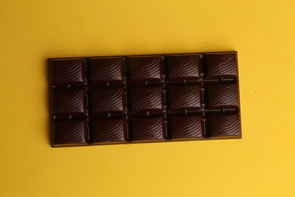 A high angle view of a dark chocolate bar isolated on a yellow background - Φωτογραφία, εικόνα