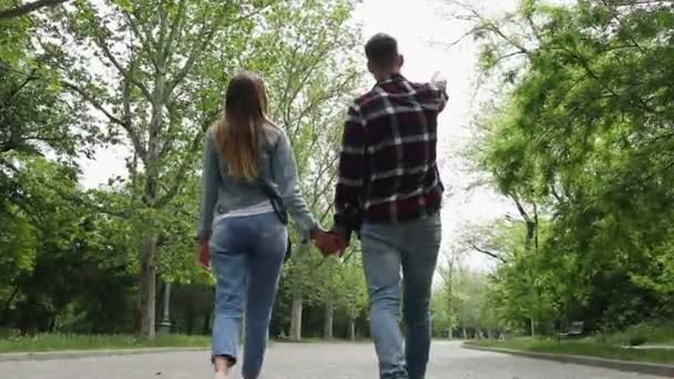 Ένα νεαρό ζευγάρι που κρατιέται χέρι-χέρι περπατά στο δρομάκι σε ένα ανοιξιάτικο πάρκο. - Πλάνα, βίντεο