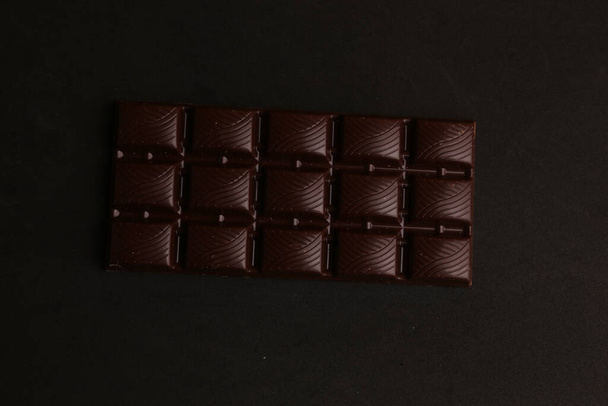A top view of a bar of dark chocolate on a black background - Fotó, kép
