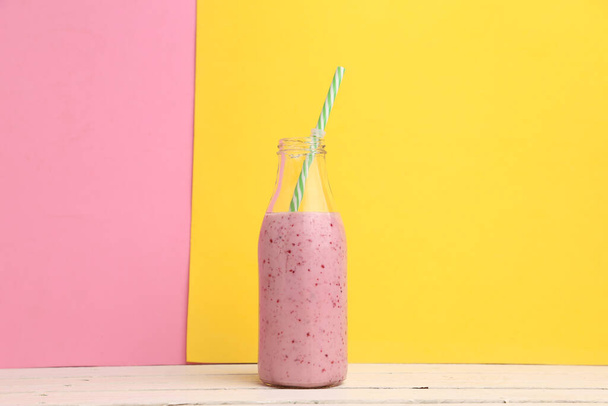 A fresh berry smoothie in a glass cup with a straw on a pink and yellow background - Фото, зображення