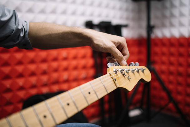 Hand of male musician tuning guitar in studio - Foto, imagen