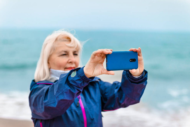Touristische kaukasische blonde Frau hält Smartphone mit leerem Bildschirm am Sandstrand der Insel, Sommerurlaub. - Foto, Bild