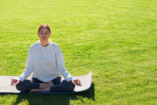 Una mujer practica yoga al aire libre en la hierba. Salud mental, reducción de la ansiedad, paz interior - Foto, Imagen