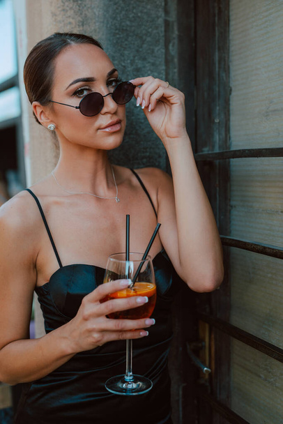 Portrait of a young beautiful woman with sunglasses and a cocktail in her hand - 写真・画像