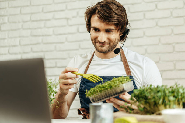 Handsome bearded man sells plant sprouts and seedlings online using laptop - Фото, изображение