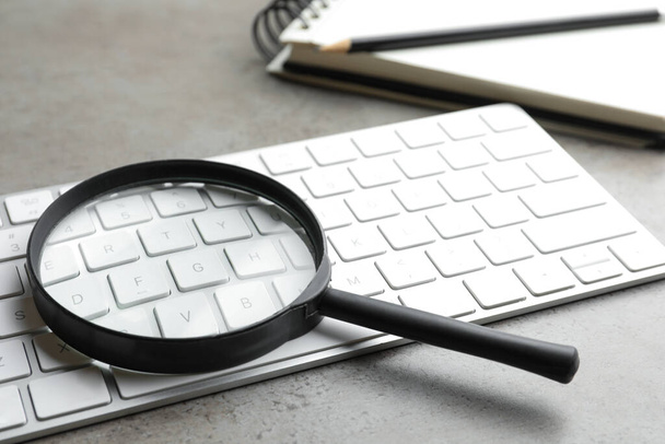 Magnifier glass and keyboard on light grey stone background, closeup. Find keywords concept - Foto, Imagem