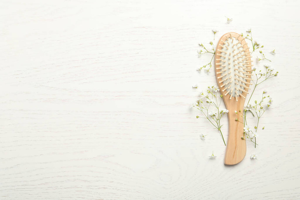Hair brush and small flowers on white wooden background, flat lay. Space for text - Foto, Imagem