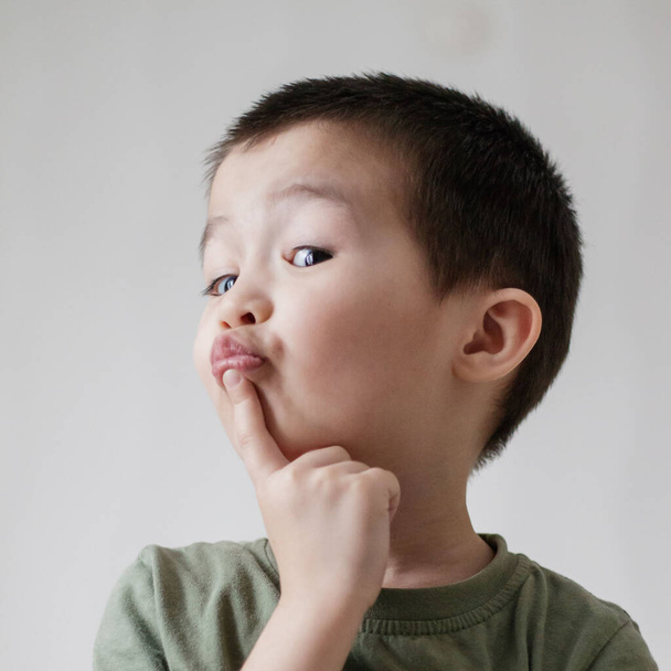 Suloinen aasialainen poika laittoi sormensa huulilleen ja katsoi alas kuin ajattelisi: - Valokuva, kuva