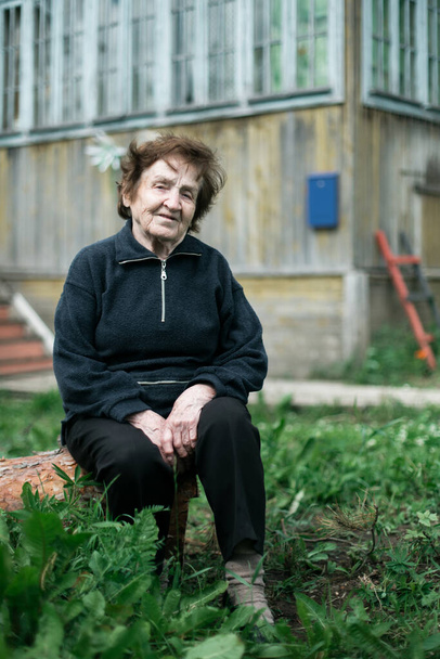 Portré egy idős nőről, aki egy vidéki ház udvarán ül.. - Fotó, kép