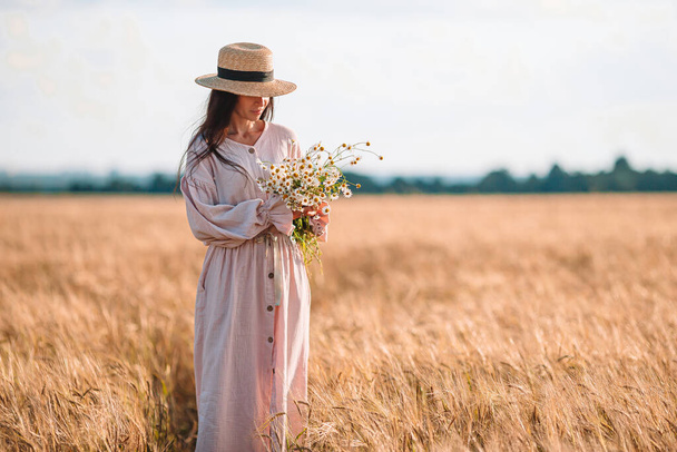 Pohled na dívku v pšeničném poli. Krásná žena v šatech v slamáku - Fotografie, Obrázek