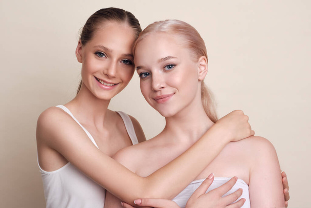 Beauty Models Portrait. Cheerful girls stick their hands together and laugh. Girls with natural makeup stand together on a beige background - Фото, зображення
