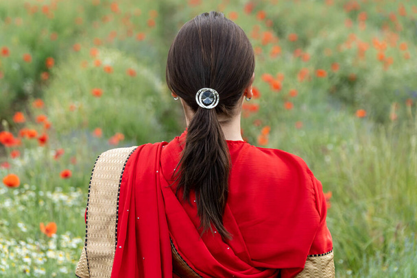 Young woman dressed in a traditional Indian costume called Sari walking in a red poppy flower field - Fotoğraf, Görsel