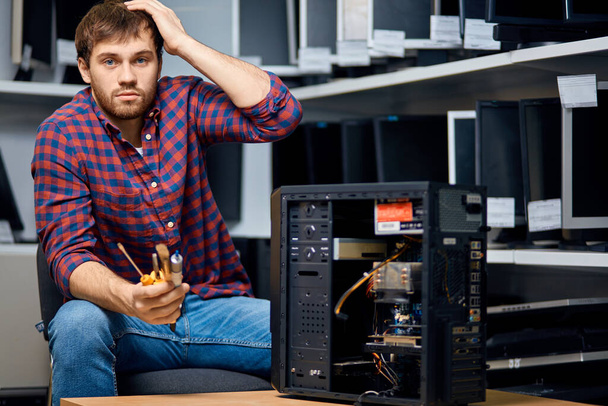 thoughtful confused bearded guy sitting near the broken system unit - Фото, изображение