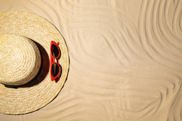 Straw hat and sunglasses on sand, top view. Beach accessories - Fotoğraf, Görsel