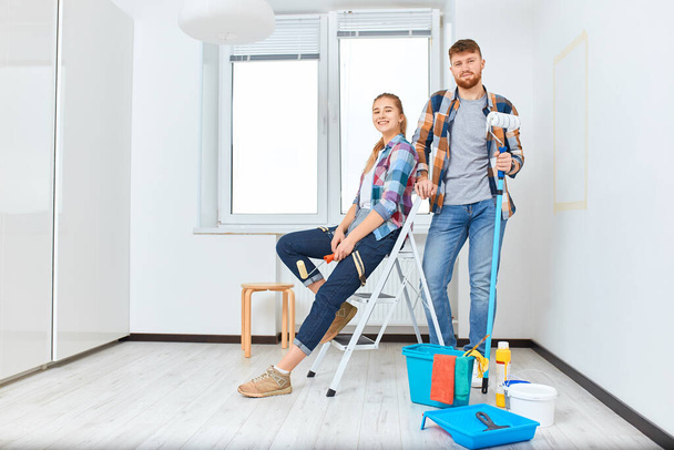 Smiling couple painting at home, holding paint roller and brush isolated - 写真・画像
