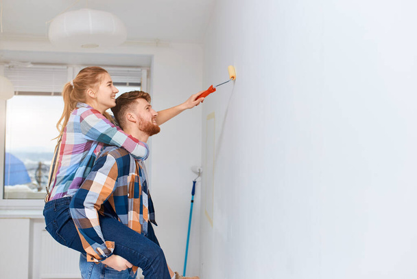 Vrouw meeliften op haar man om extra hoogte te krijgen bij het schilderen van huis muur - Foto, afbeelding
