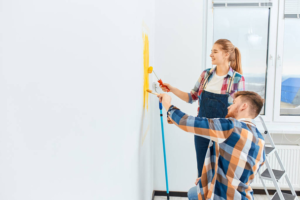 Couple in casual plaid shirts paint house wall together. DIY renovation concept. - 写真・画像