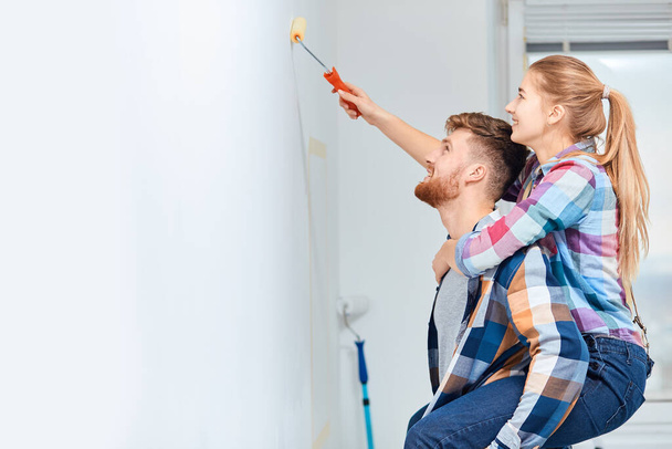 Woman piggybacking on her husband to gain extra height when painting home wall - Фото, изображение