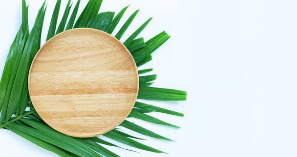 Empty wooden plate on tropical palm leaves on white background. Top view - Foto, imagen