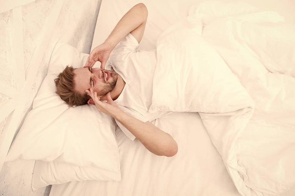 Migraine headaches. Handsome man relaxing in bed. Snoring can increase risk headaches. Common symptom of sleep apnea. Causes of early morning headache. Sleep problems can lead to headaches in morning - Фото, изображение
