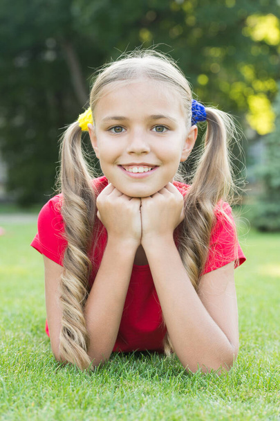 Little girl cute ponytails hairstyle relaxing on green grass, summer camp concept - Photo, image