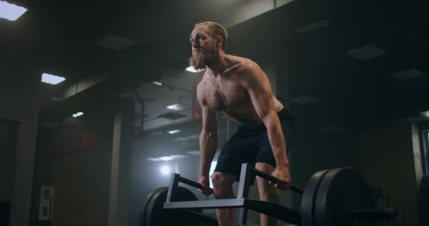 Un hombre levantando pesas pesadas en el gimnasio. Los montacargas rumanos con una barra en el gimnasio en cámara lenta - Metraje, vídeo