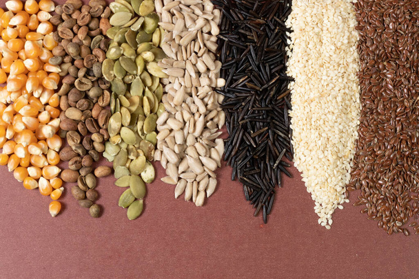 Diferentes cereales y semillas - maíz, calabaza, café, quinua, pimienta, arroz, girasol de mijo - sobre una superficie marrón - Foto, Imagen