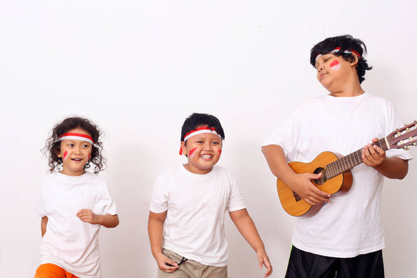 Приватні діти з Індонезії відзначають День незалежності Індонезії. Веселі вирази, одягнувши червону і білу стрічку як символ індонезійського прапора проти білої стіни. - Фото, зображення