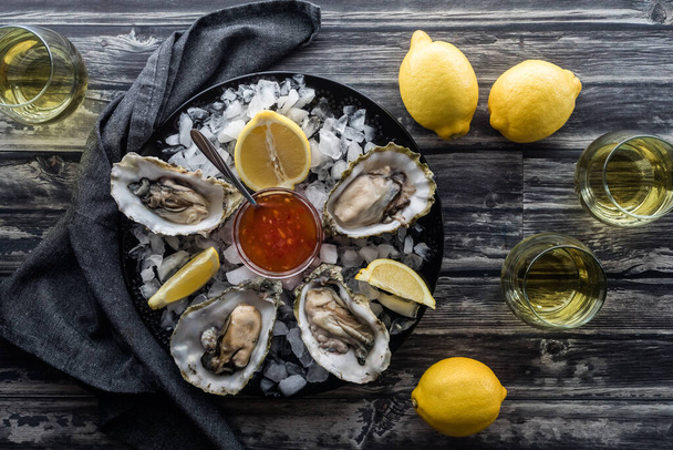 Fresh oysters on a plate of ice with lemon wedges served with glasses of white wine. - Valokuva, kuva