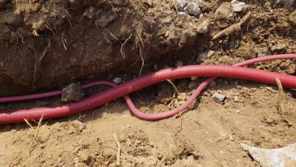 CLOSE UP: Red plastic telecommunication conduits run along a shallow trench. - Footage, Video