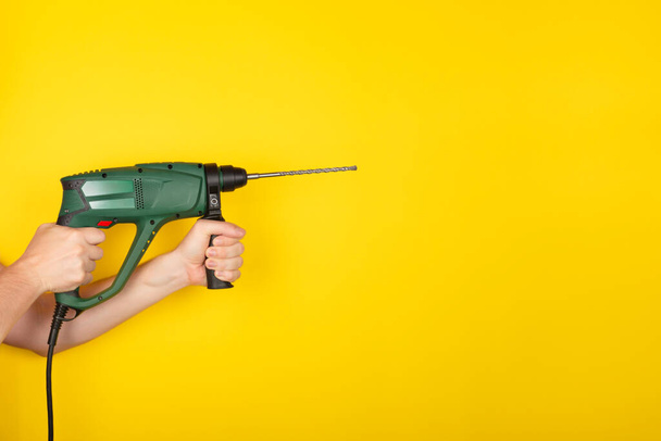 Green Puncher en manos de un constructor. Las manos masculinas sostienen el nuevo perforador o taladro aislado sobre fondo amarillo. Banner con espacio de copia - Foto, imagen
