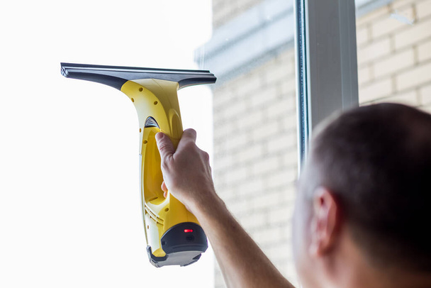 Cleaning windows with vacuum cleaner.worker cleaning glass window of modern building.Men hand with with portable professional electric vacuum cleaner. - Zdjęcie, obraz