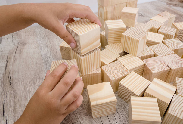 Две руки играют с деревянными кубиками на деревянном фоне. - Фото, изображение