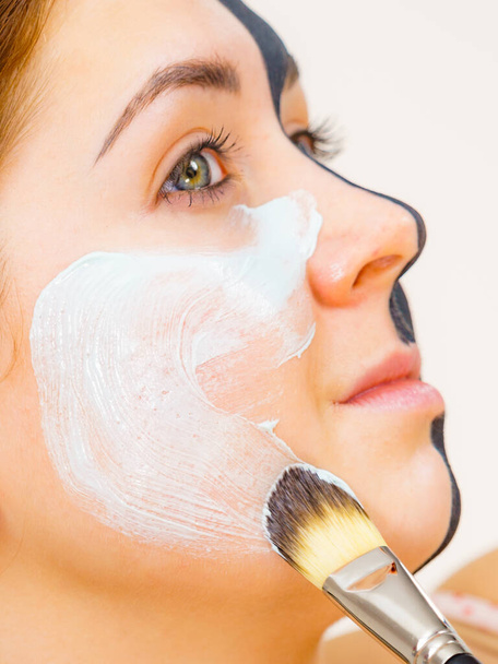 Woman with clay carbo black mask on half face applying white mud to clean skin. Girl taking care of oily complexion. Beauty procedures. Skincare. - Foto, imagen