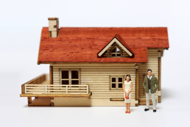 Un uomo e una donna in miniatura di fronte a una casa in legno in miniatura. - Foto, immagini