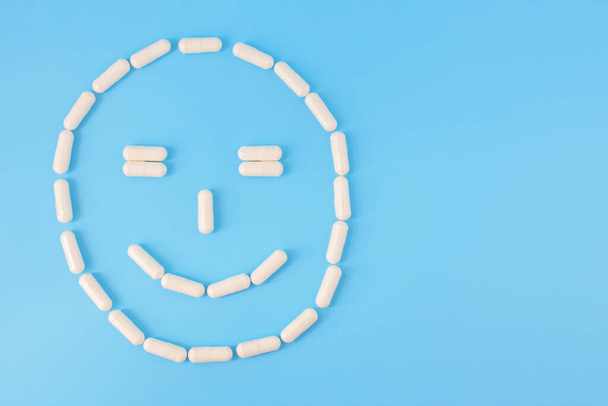 Capsules arranged in smilng face. Smiling face made from white pills on a blue background. The concept of good health, recovery from illness, healing, founding a cure Copyspace. - Photo, image