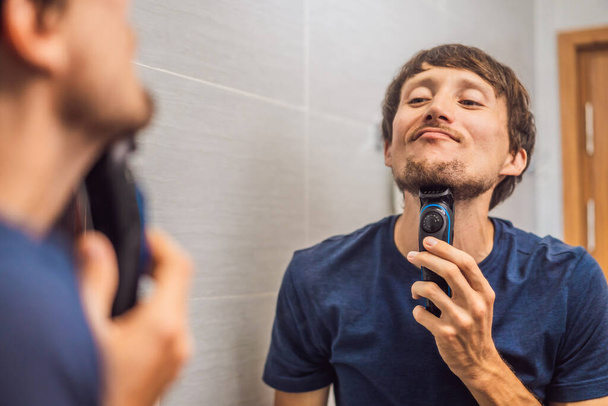 Handsome young bearded man trimming his beard with a trimmer - Foto, immagini