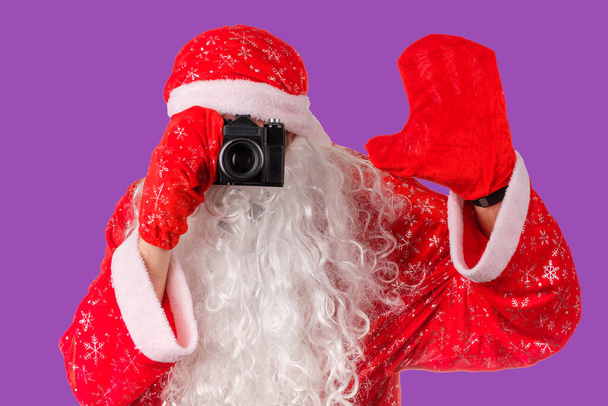 Noel Baba eski bir kamerayla fotoğraf çeker. Noel fotoğrafı eflatun arkaplan - Fotoğraf, Görsel