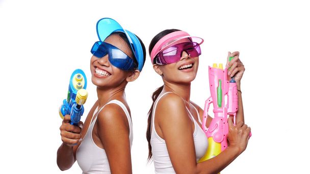 Portrait of two beautiful Asian women in pink and blue sun visor cap and sunglasses posing with water guns over white background - Photo, Image