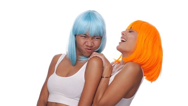 Retrato de duas belas mulheres asiáticas felizes amigos em azul brilhante e peruca laranja posando sobre fundo branco
 - Foto, Imagem